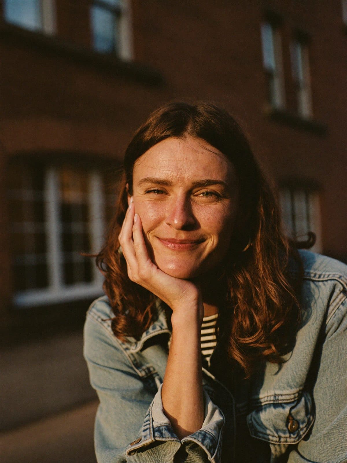A woman in warm golden light, hand resting against her cheek